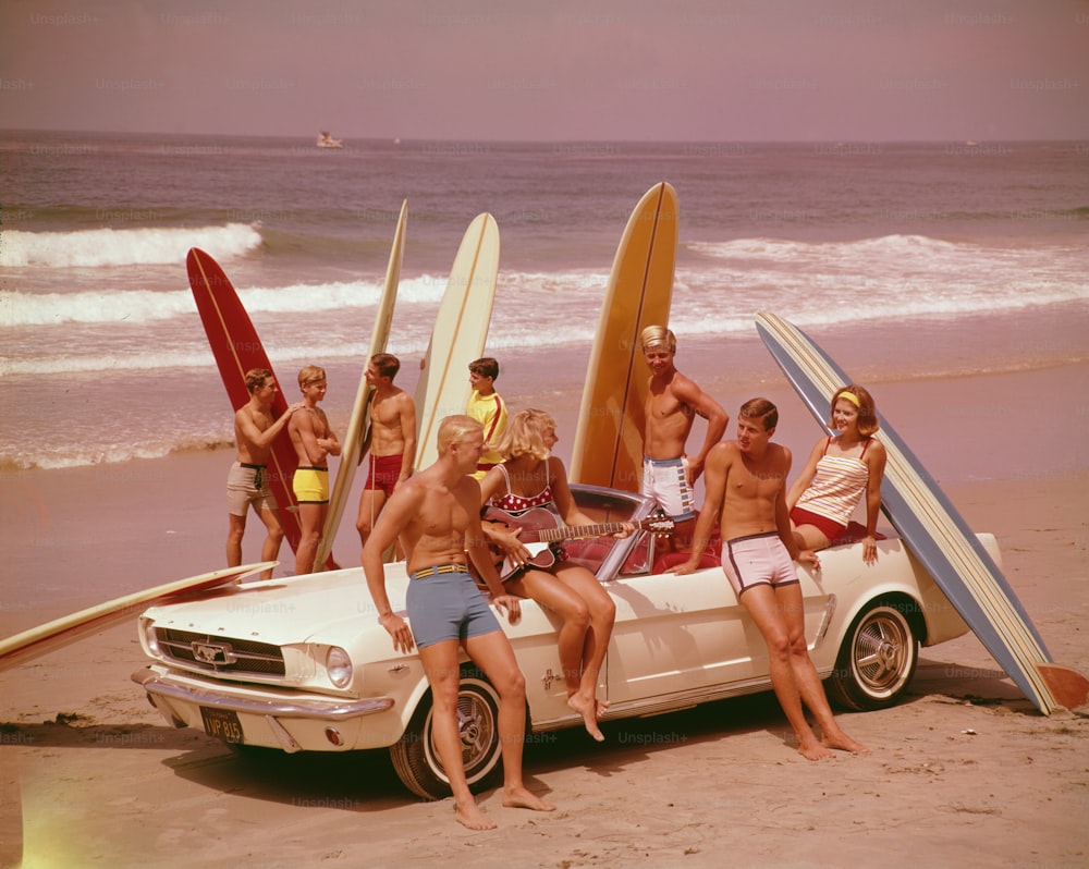 A group of surfers on a beach with a Ford Mustang car.