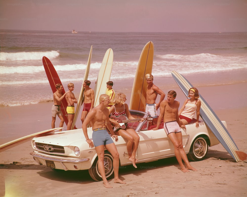 Eine Gruppe von Surfern an einem Strand mit einem Ford Mustang.