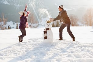 Un hombre y una mujer construyendo un muñeco de nieve en la nieve