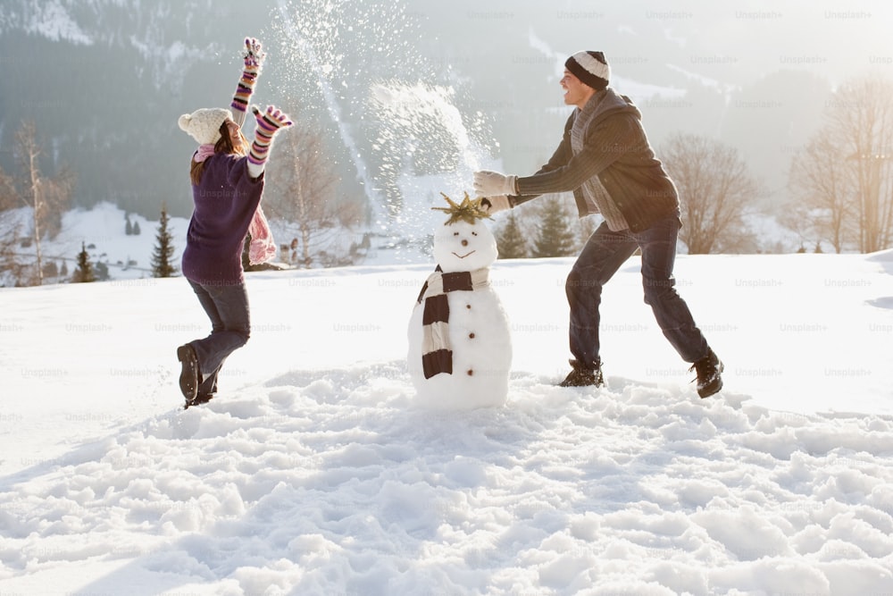 Ein Mann und eine Frau, die einen Schneemann im Schnee bauen
