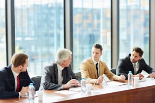 Ejecutivos de negocios modernos y seguros de sí mismos en trajes formales sentados en la mesa de conferencias y discutiendo en la reunión mientras discuten el desarrollo de la empresa