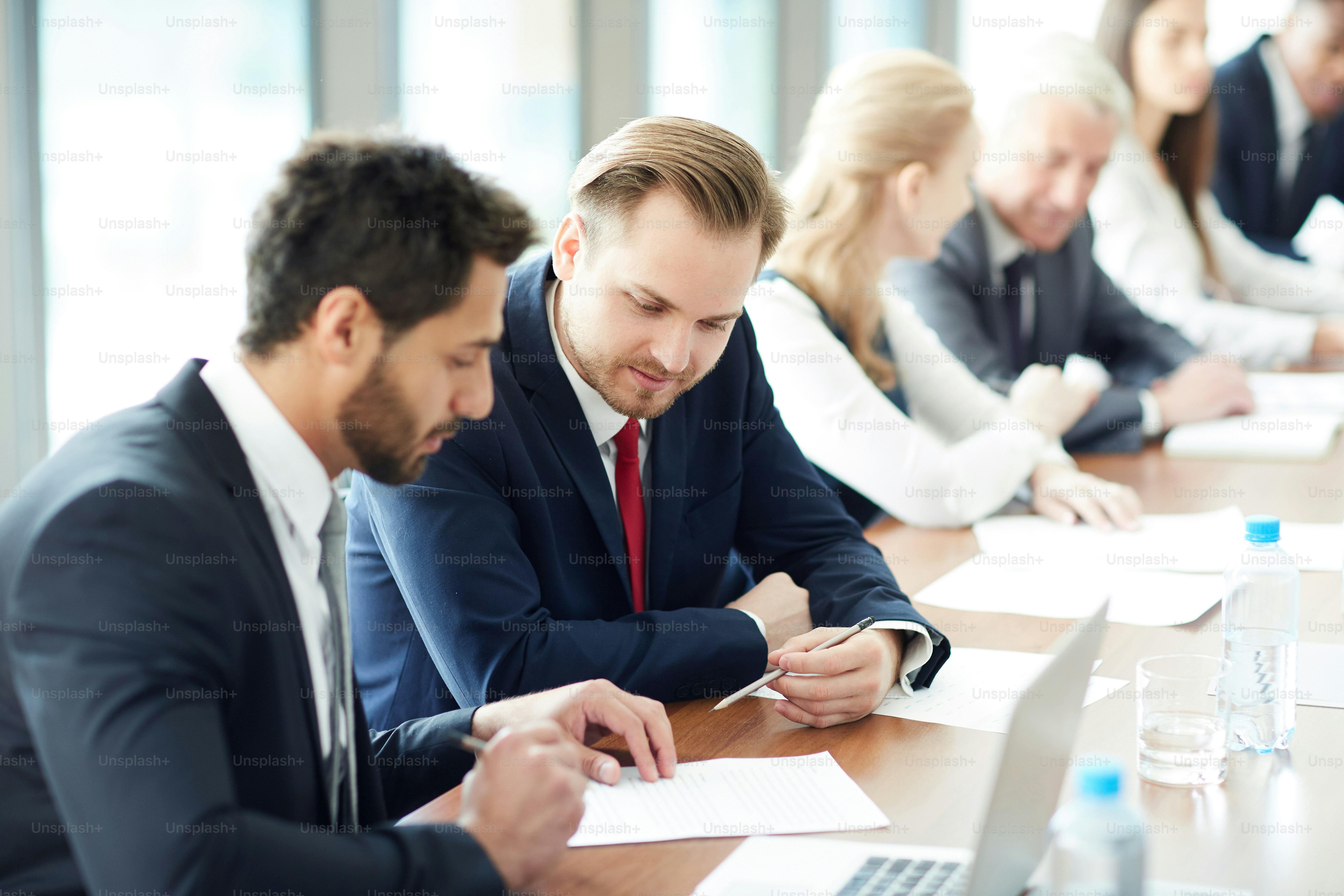 Pensive multiethnic conference participants reading information on paper and discussing task at business class