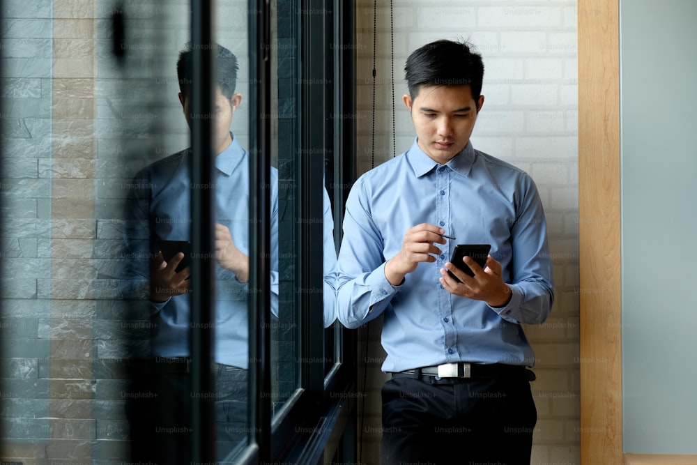Confident young Asian businessman working on digital tablet while standing in office