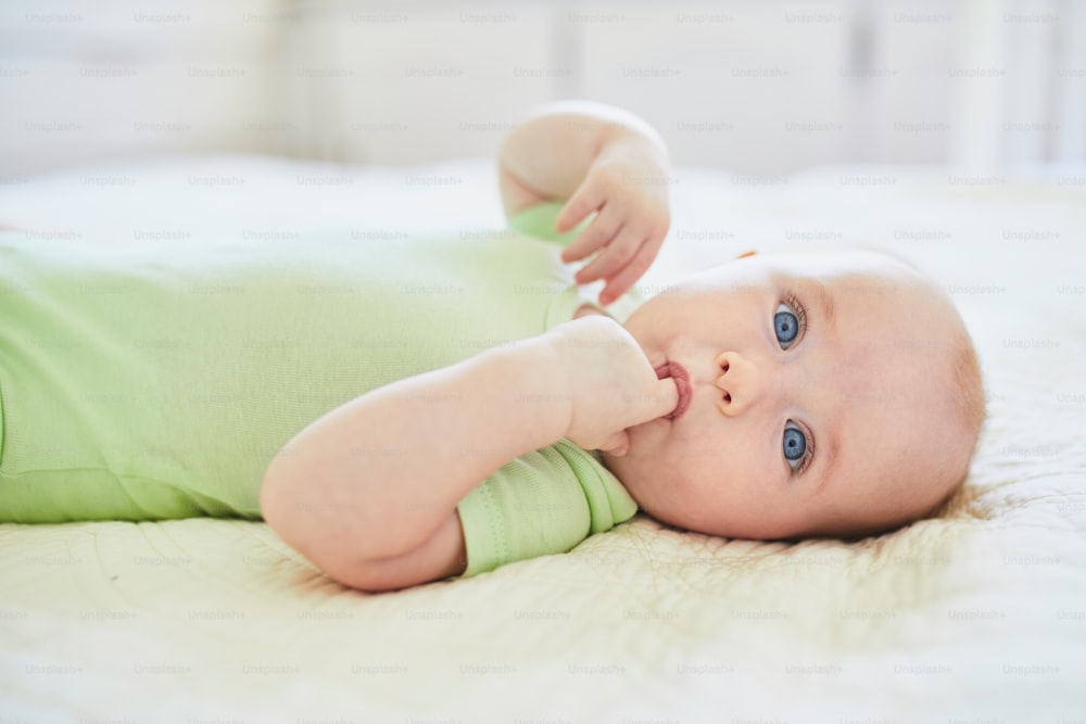 Bambina che si succhia il dito per consolarsi. Bambino piccolo sdraiato sul letto. Bambino neonato in asilo nido soleggiato