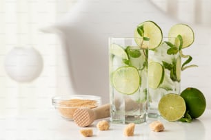 Two mojito cocktails with lots of ice, white rum, lemon juice and tonic, decorated with lime slices and mint leaves on a modern white table