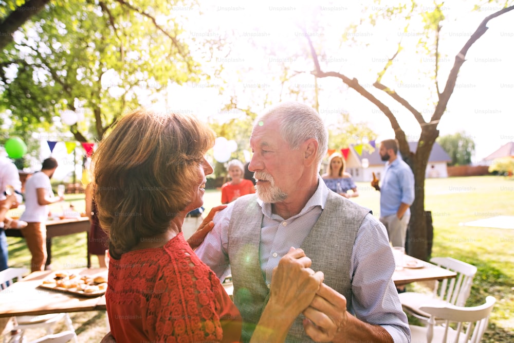 A senior couple dancing on a garden party or family celebration outside in the backyard.