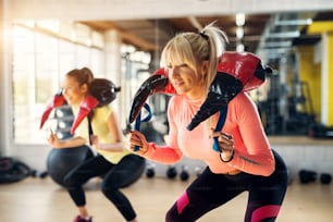 Two focused fit girls doing squats with weight equipment around their necks.