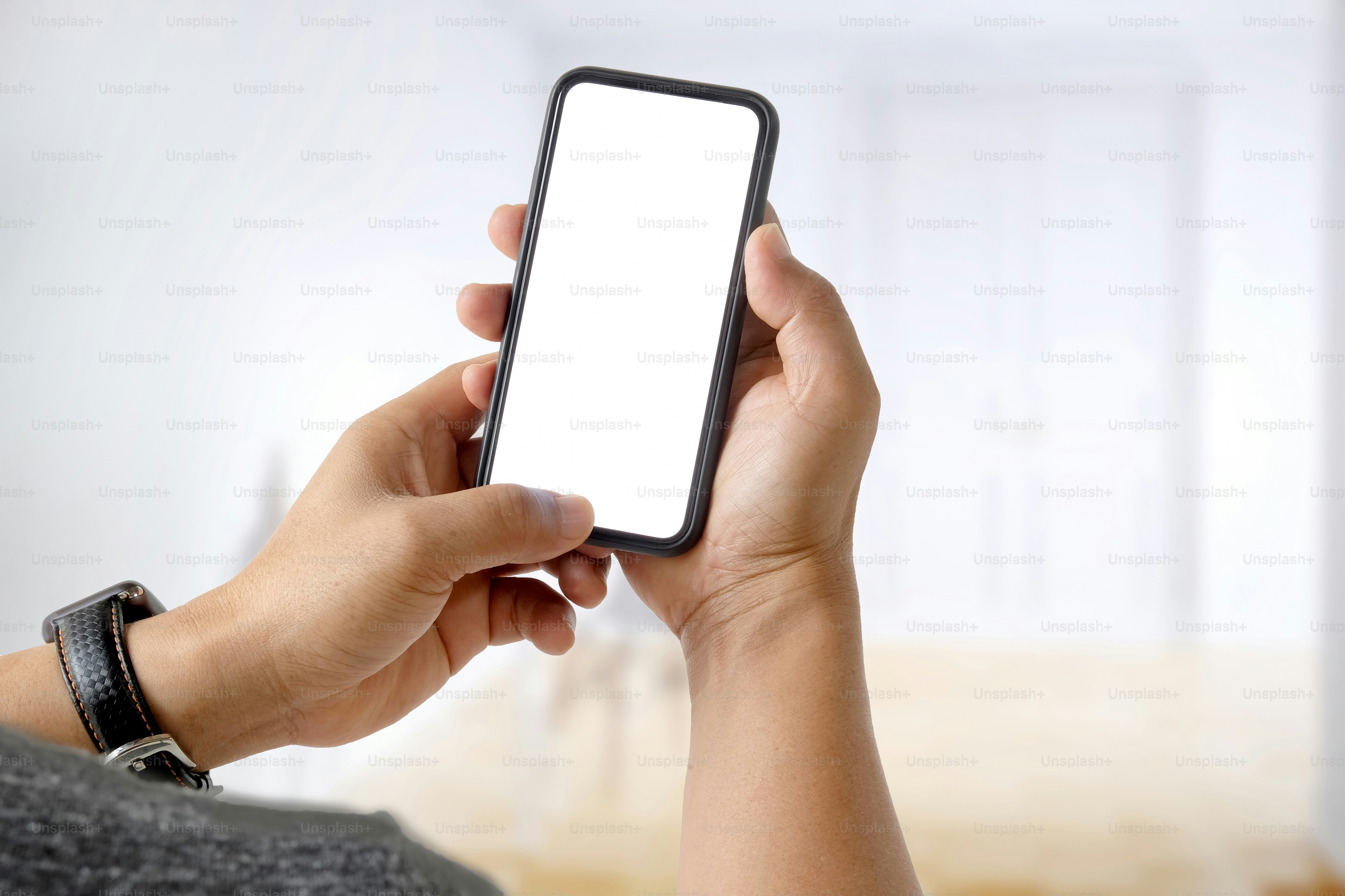 Primer plano de un hombre usando un teléfono inteligente móvil de pantalla en blanco sobre un fondo bokeh borroso.