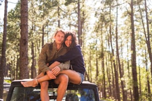 Paar in Freundschaft und Liebe sitzen auf dem Dach des Autos während eines Reiseurlaubs. Geparkt im Wald mit hohen Kiefern und Bäumen im Hintergrund. Genießen Sie die Natur und Freizeitaktivitäten im Freien.