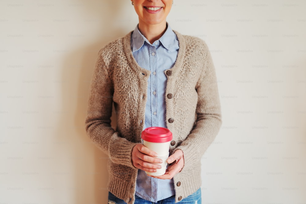 Close up of young hipster females hands holding a cup of coffee. Girl standing against the wall.