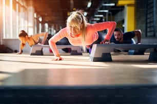 Three strong young athletes doing some push ups with one hand on a stepper.