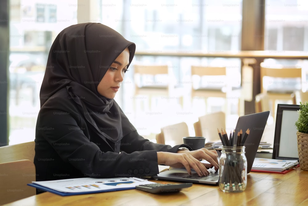 Atractiva trabajadora corporativa árabe que trabaja en la computadora portátil en el escritorio