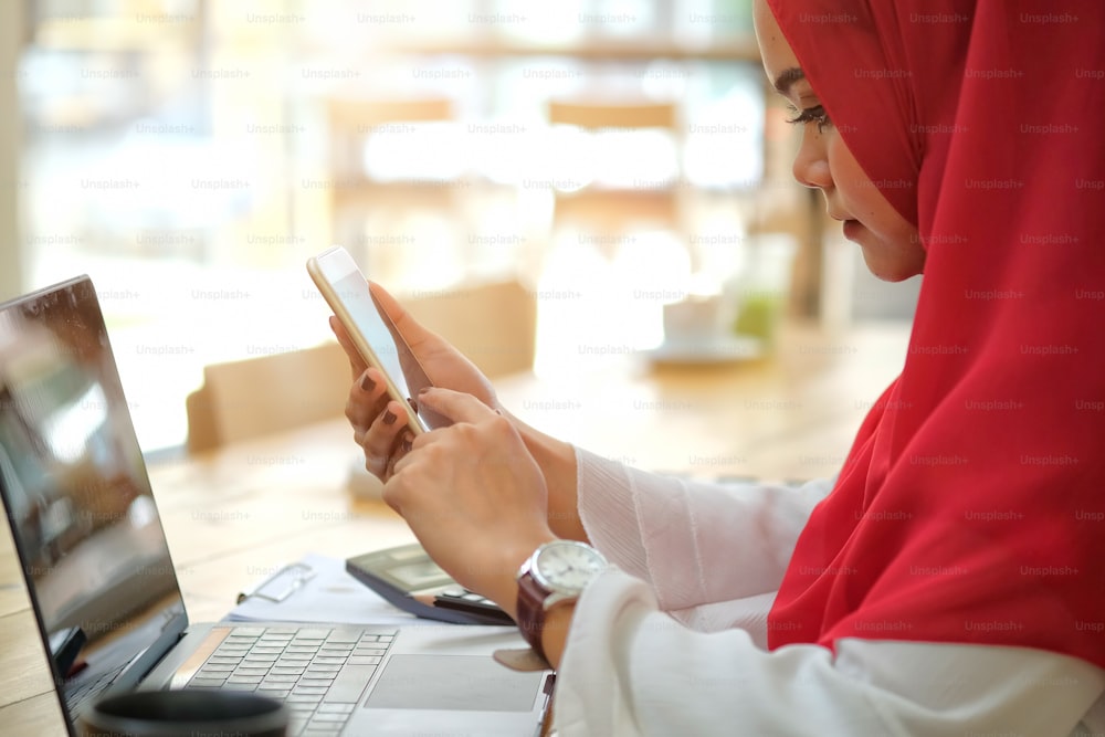 Giovane donna d'affari musulmana che utilizza il suo smartphone mobile alla scrivania dello spazio di lavoro.