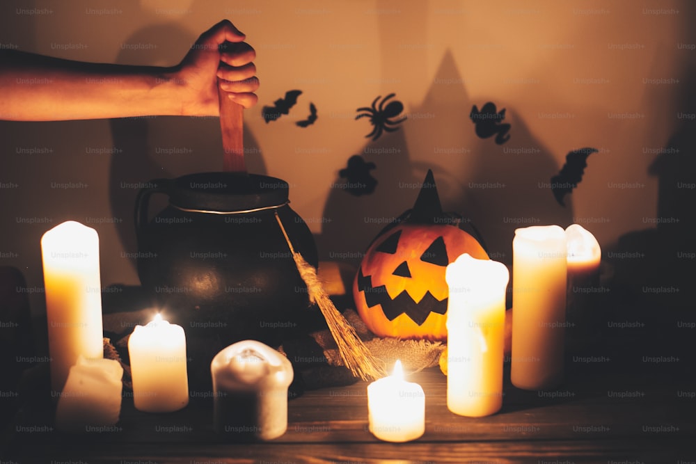 Happy Halloween. witch hand boiling potion for spell, with jack o lantern pumpkin with candles, bowl,broom and bats, ghosts on background in dark spooky room. spooky atmospheric moment