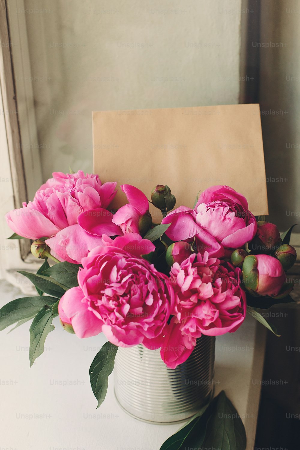 precioso ramo de peonías rosas con tarjeta de artesanía vacía en la ventana antigua de madera blanca rústica a la luz, vista superior, espacio para texto. Maqueta de tarjeta de felicitación floral. Concepto de feliz día de las madres.