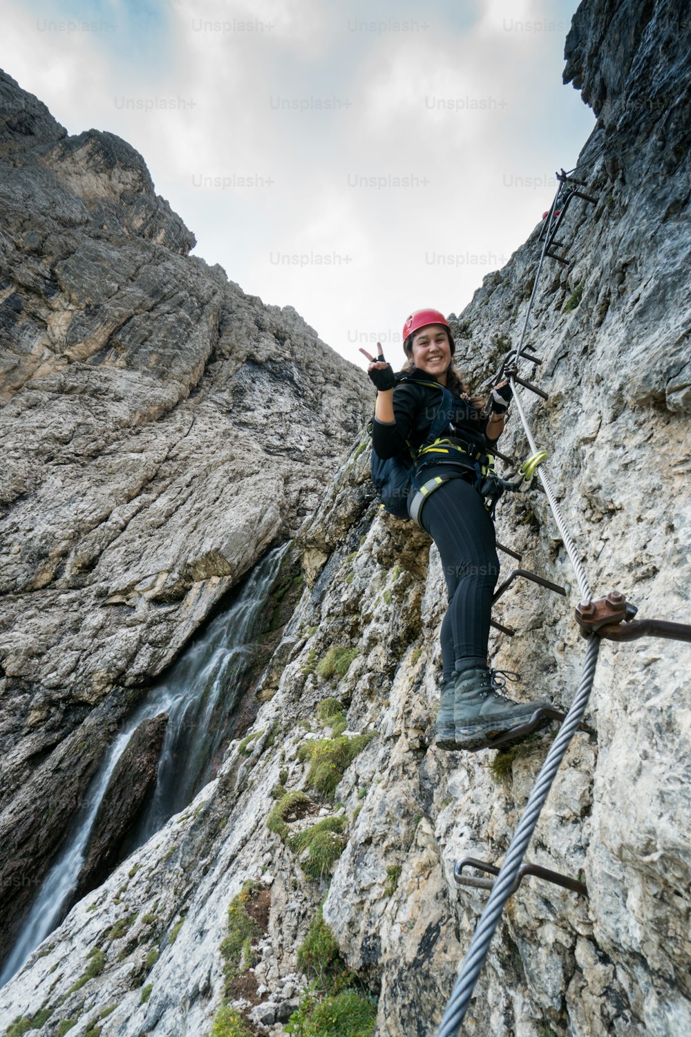 young attractive female mountain climber on a difficult Via Ferrata in the Dolomites in Alta Badia in the South Tyrol in Italy smiling and making a peace sign