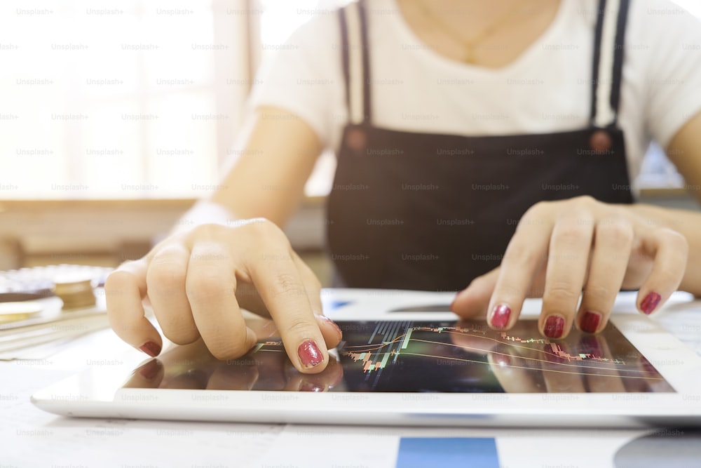 Foto recortada de Mujer tocando gráfico del mercado de valores en un dispositivo de pantalla táctil en casa. Negociación en concepto bursátil.
