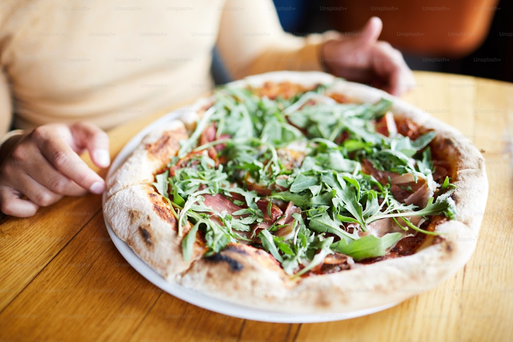Appetizing pizza with fresh herbs and bacon on plate in front of hungry person