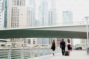 Business colleges walking through Dubai Marine after finishing job for that day. Group of Afro-American man and two European ladies.