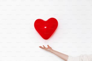 空中でハートを握る手。ハッピーバレンタインデーのコンセプト。白い背景に赤いハートの吹き出しとテキスト用のスペース。 ヘルスケア、医学、献血のコンセプト。愛と保護