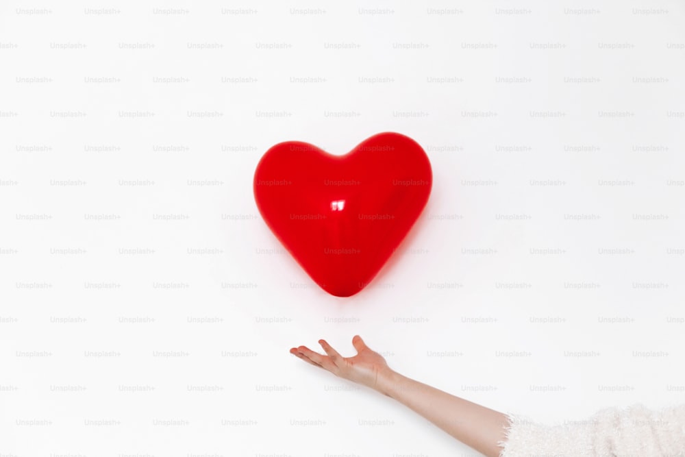 공중에서 심장을 잡고 손. 행복한 발렌타인 데이 개념입니다. 텍스트를 위한 공간이 있는 흰색 배경에 빨간색 하트 풍선.  건강 관리, 의학 및 헌혈 개념. 사랑과 보호