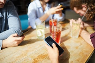 화창한 날 나무 테이블 옆에 앉아 음료를 마시면서 스마트폰을 사용하는 젊은이들