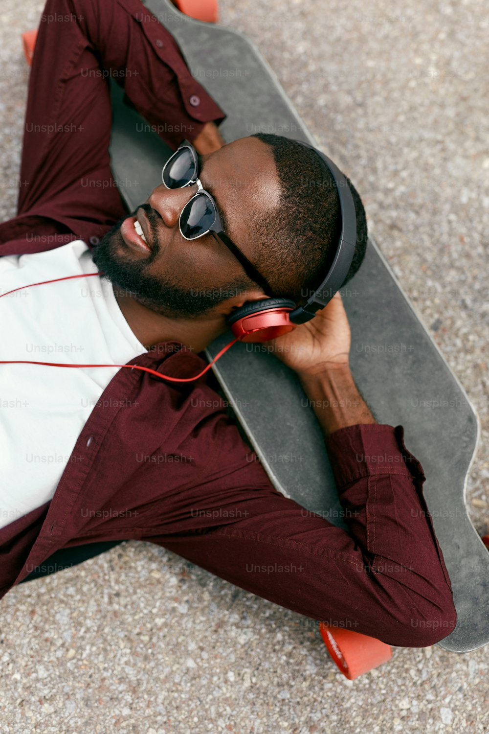 Mode. Homme noir écoutant de la musique dans des écouteurs dans la rue, allongé sur un longboard. Haute résolution