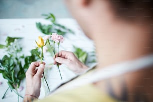 새로운 구성을 위해 꽃을 선택하는 꽃집의 손에 노란색 장미와 옅은 분홍색 카네이션