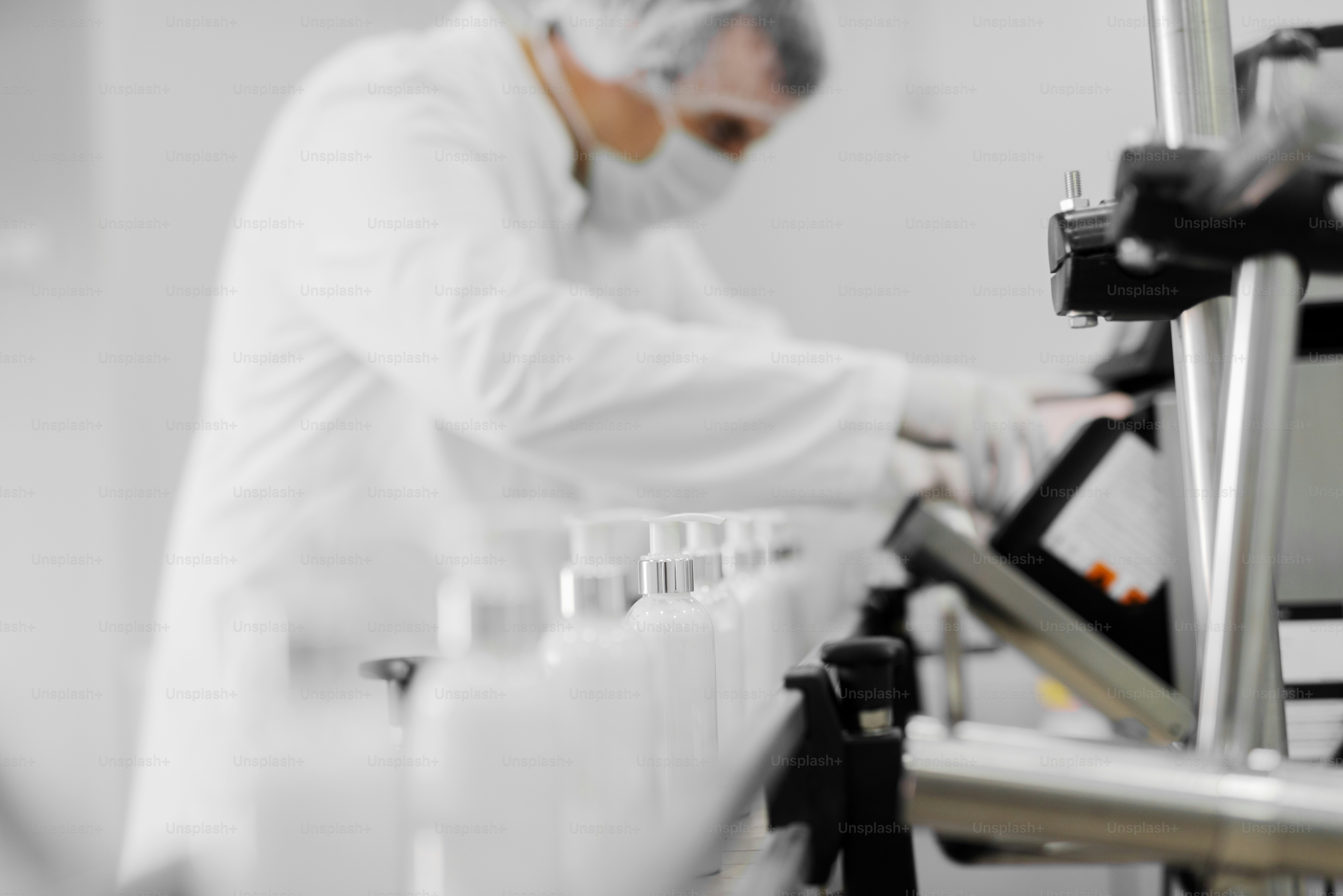 A person in a white lab coat and mask operating a bottle filling machine