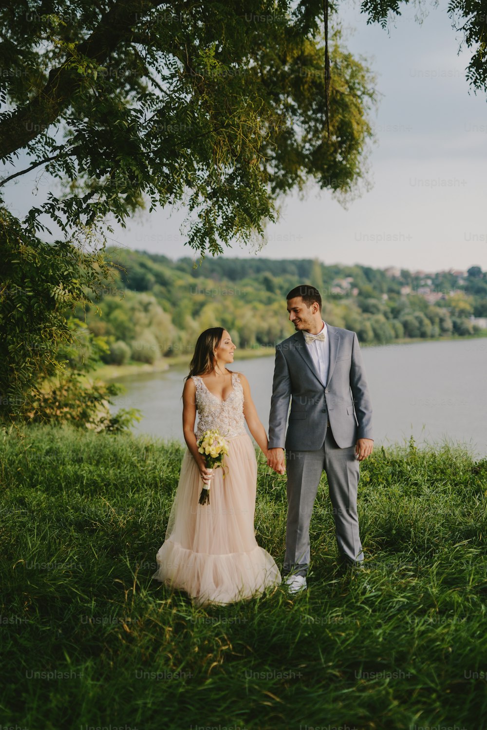Dia do casamento. Lindo casal jovem bonito em seu dia de casamento em pé na natureza perto do rio e olhando um para o outro.