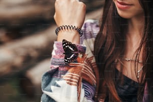 beautiful butterfly on girl hand. stylish hipster,happy woman in hat holding apatura iris  on fingers in forest in mountains. travel and wanderlust concept. space for text. amazing moment