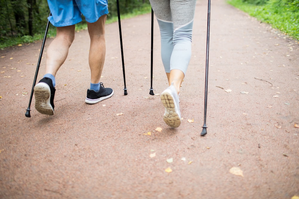 Legs of mature active couple walking down road in park during trekking workout