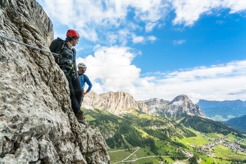 two young mountain climbers  on a steep and exposed climb in the Dolomites of Alta Badia in Italy with a great view of the Val Gardena behind them