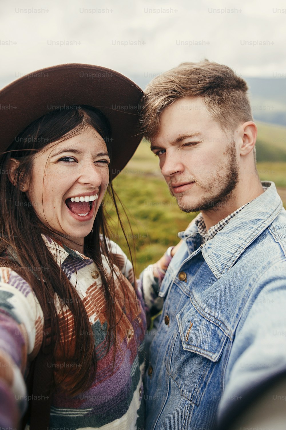stylish hipster couple having fun and taking selfie on top of sunny mountains. happy family smiling. summer vacation. space for text. atmospheric moment. travel and wanderlust