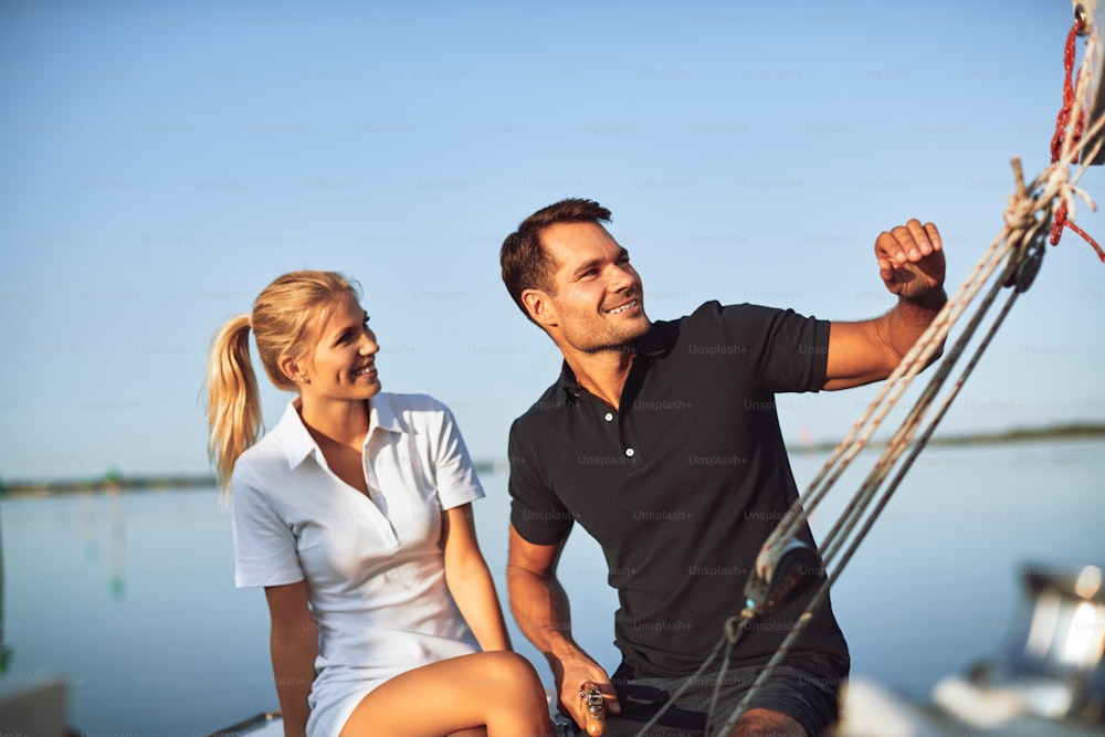 Lächelndes junges Paar, das einen Nachmittag zusammen genießt, während es auf dem Deck seiner Yacht sitzt