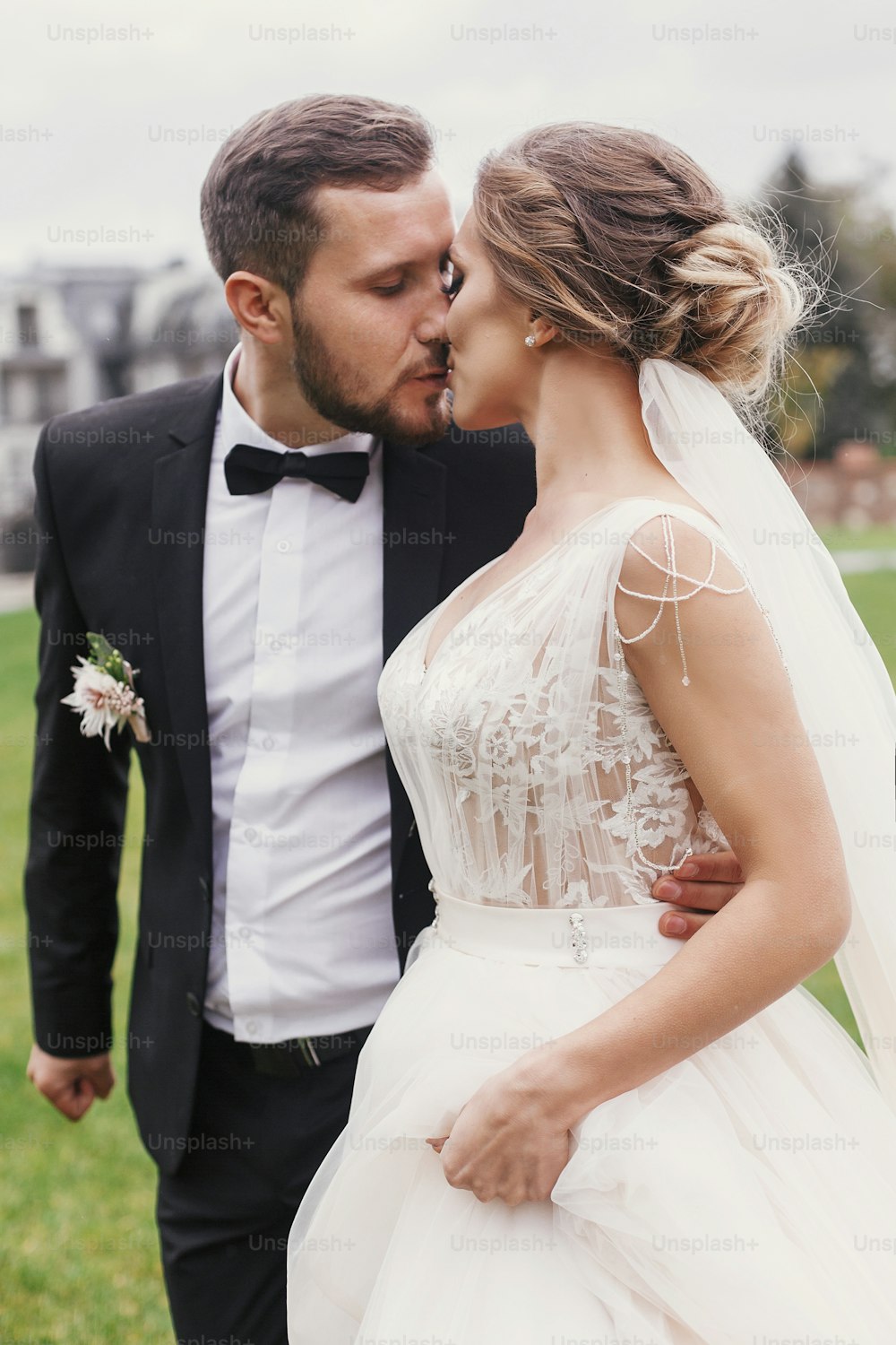 Gorgeous bride and stylish groom gently hugging and kissing outdoors. Sensual wedding couple embracing. Romantic moments of newlyweds. Wedding photo