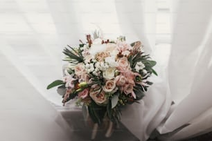 Stylish wedding bouquet of pink roses and green eucalyptus on background of window. Modern bride's bouquet on soft fabric in morning light. Wedding arrangements and decor