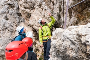 A male mountain guide instructs young climbers at the start of a steep Via Ferrata in the Dolomites of northern Italy in Alta Badia