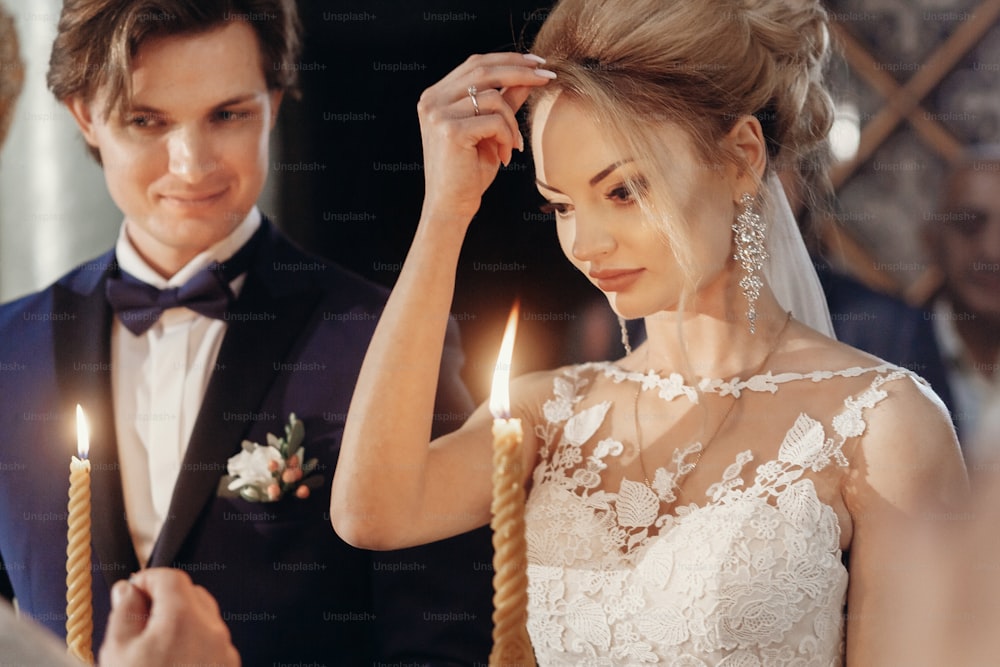 Beautiful bride and groom holding candles during wedding ceremony in church, gorgeous blonde bride and handsome groom performing spiritual ritual, marriage concept