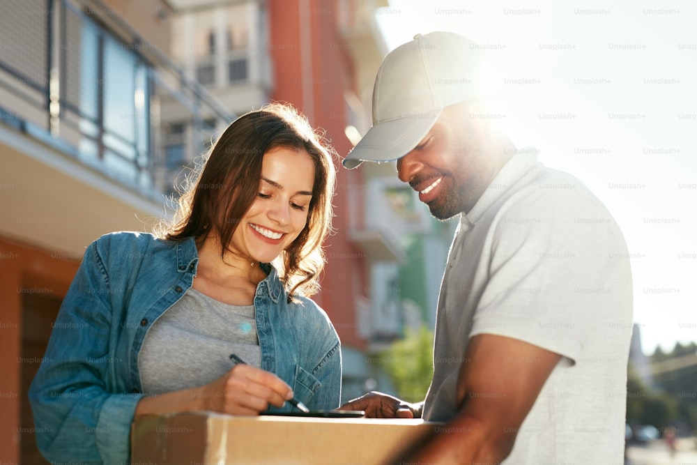 Courier Delivery Service. Man Delivering Package To Woman, Signing Documents On Box. High Resolution