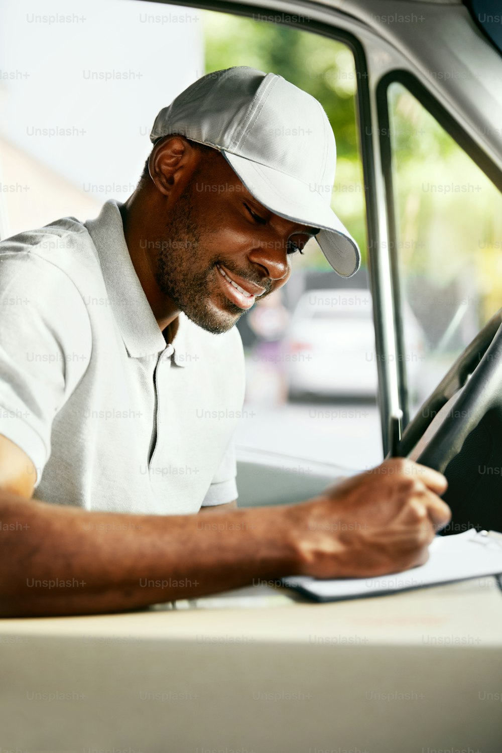 Correio. Entregador lendo endereços sentado na van de entrega. Trabalhador negro do sexo masculino arquivando documentos no carro. Alta Resolução