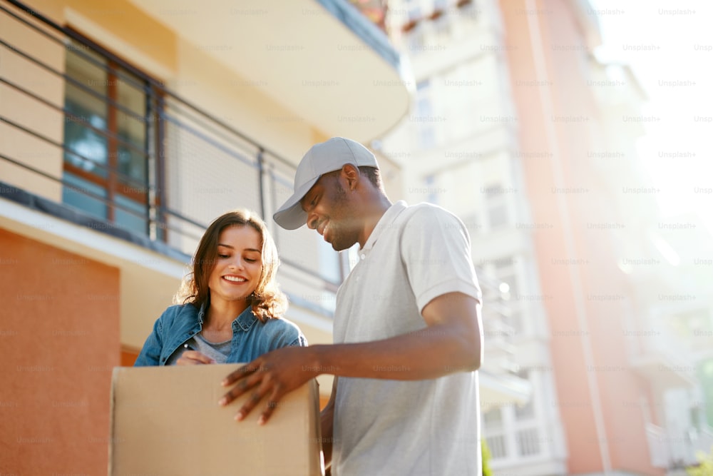 Package Delivery. Man Courier Delivering Box To Woman At Home. Female Receiving Parcel Outdoors, Signing Documents. High Resolution