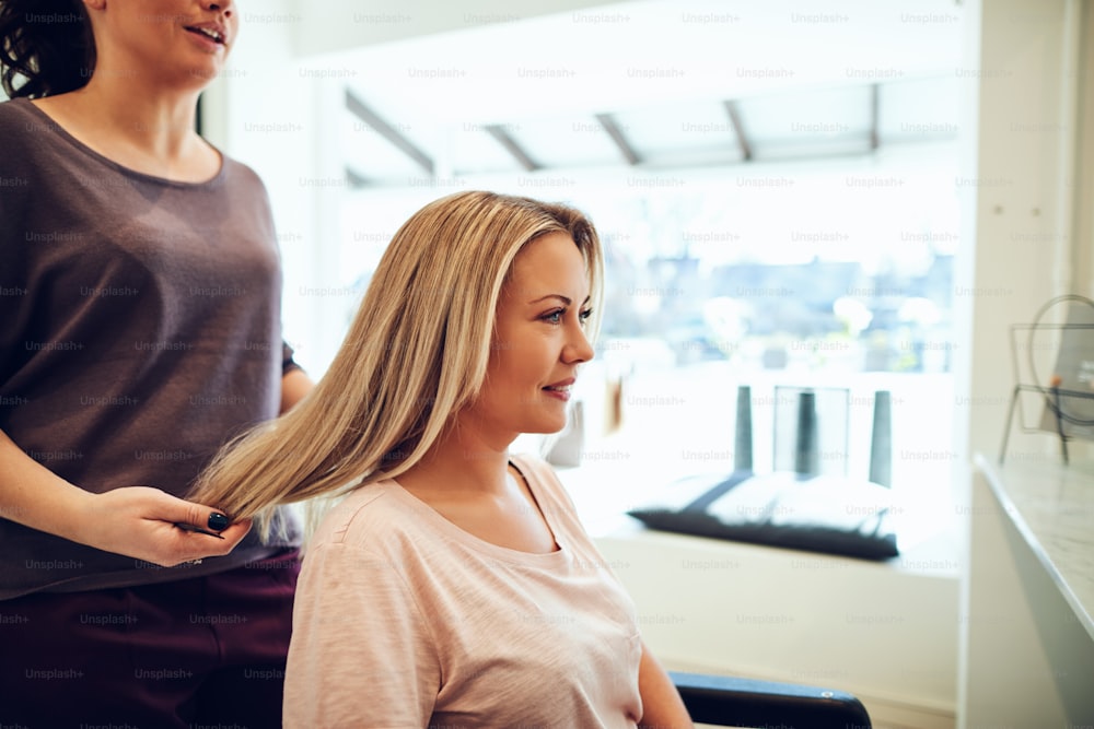 Smiling young blonde woman sitting in a salon chair having her hair done during an appointment with her hairstylist