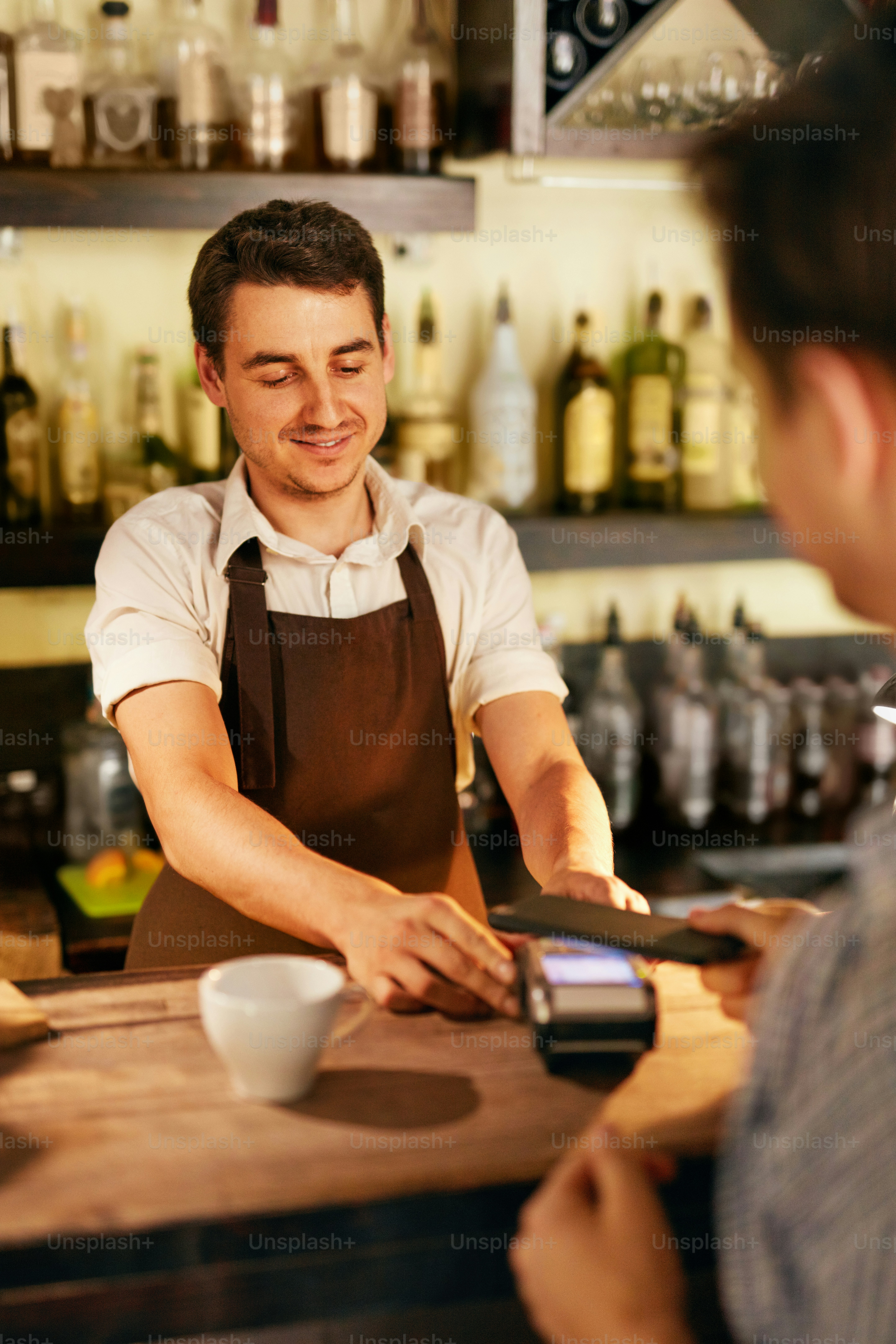 Customer Paying With Mobile Phone In Cafe. Bartender With Pay Terminal