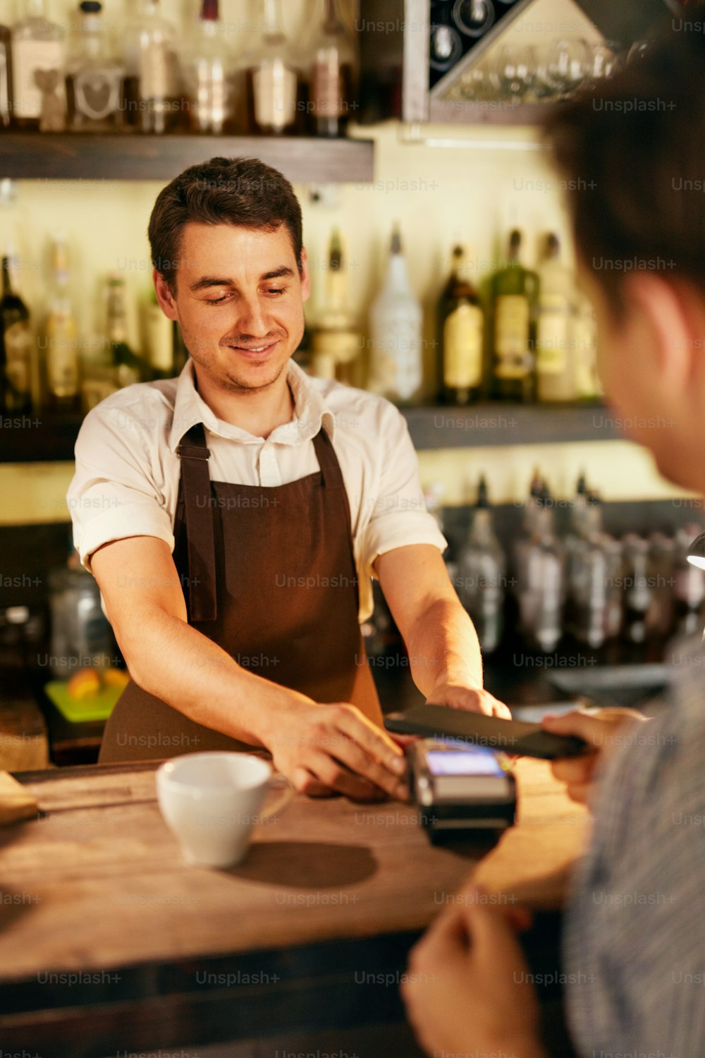 Customer Paying With Mobile Phone In Cafe. Bartender With Pay Terminal At Bar Counter. High Resolution