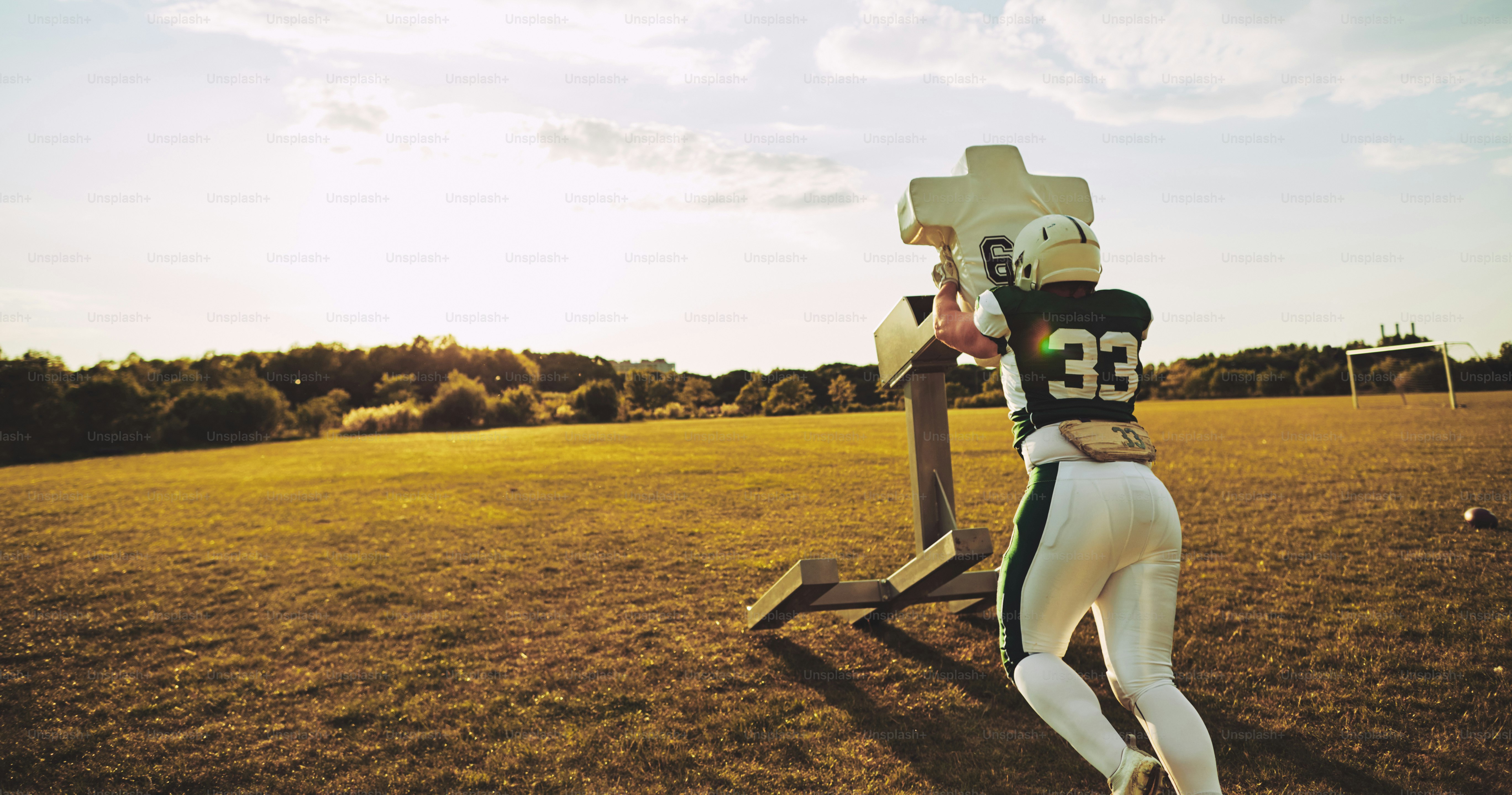 Young American football player doing tackles and defensive drills outside on a sports field in the late afternoon