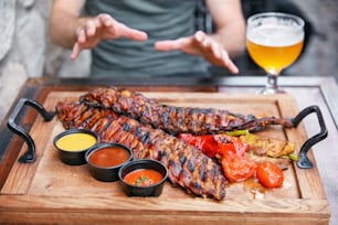 Barbecue Meat With Vegetables And Beer In Restaurant. Man Eating Grill Pork Ribs Closeup. High Resolution