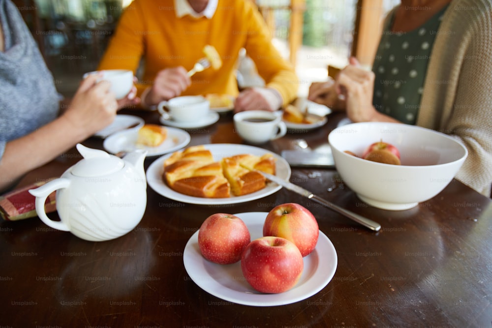 Tea party with desserts: close-up of wooden table with teapot, sweet pie and apples, friends having breakfast together