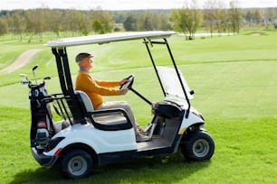 Hombre de edad contemporánea que conduce un coche de golf a lo largo de un vasto campo verde mientras va a jugar