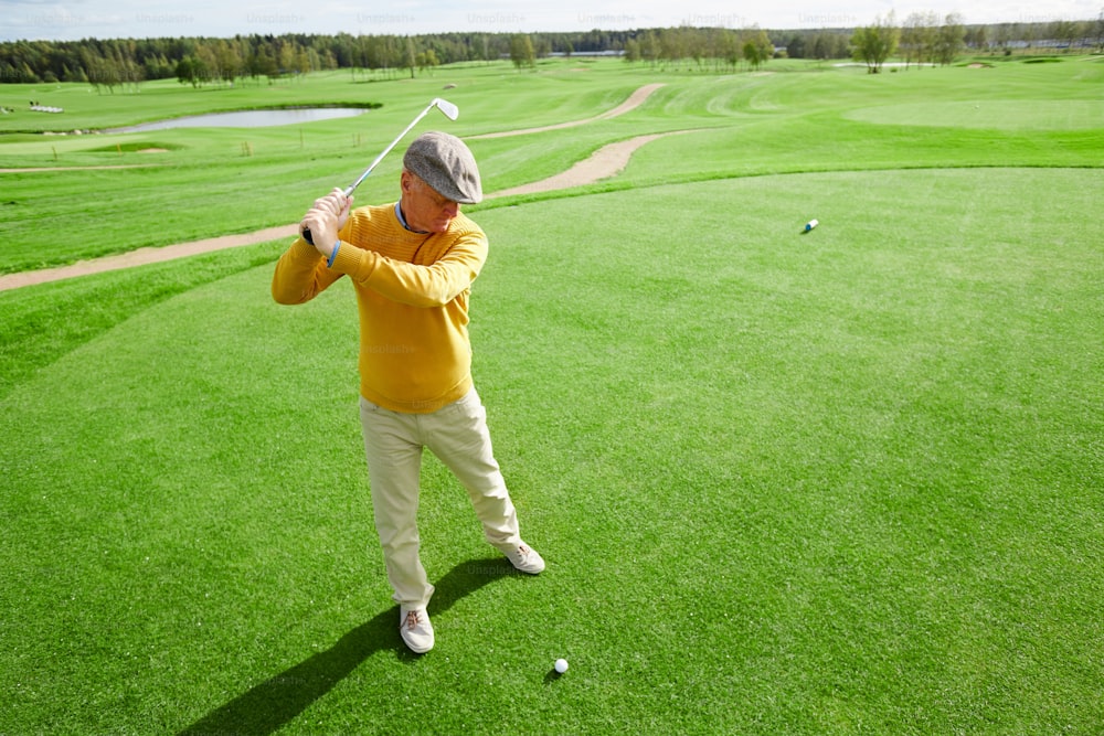 Homme âgé avec un club de golf prêt à frapper la balle couché sur l’herbe verte pendant un match de loisir